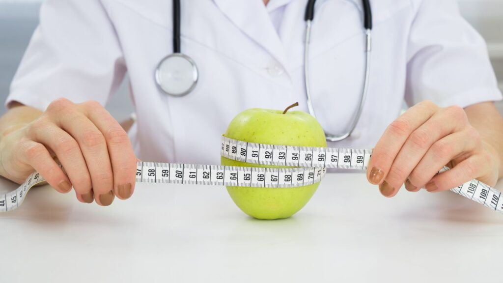 Obrazek przedstawia jabłko, które jest trzymane przez dietetyka